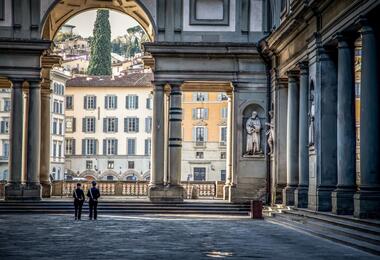 Two individuals stand before the Uffizi Gallery, showcasing its impressive pillar architecture.
