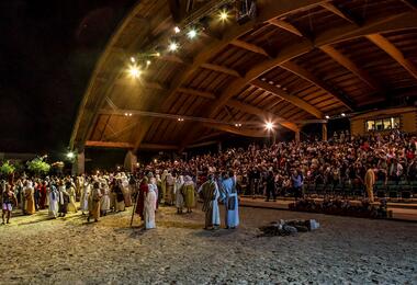 Numerous spectators stand on the sandy ground, engaged in the Sordevolo Passion Play event.