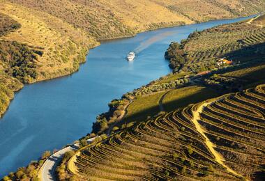 A boat glides down a river surrounded by lush green valley hills under a clear blue sky.