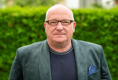 A bald man in glasses wearing a green jacket, smiling at the camera.
