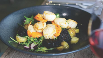 A bowl of scallops and potatoes served on a wooden table, showcasing a delicious seafood dish.