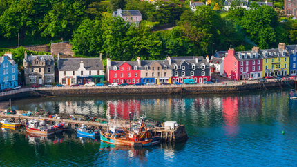 Colourful houses line the riverbank, reflecting vibrant hues in the water under a clear blue sky.