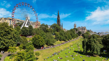 Edinburgh Castle overlooks a vibrant Ferris wheel, capturing a lively summer scene in Scotland.