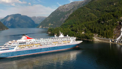 A large cruise ship sails in calm waters, surrounded by majestic mountains in the background.