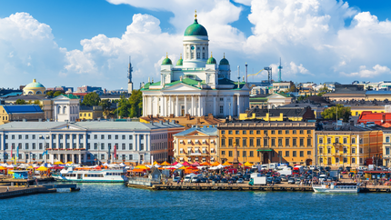 A panoramic view of a bustling city skyline with numerous buildings and boats in the foreground on the water.