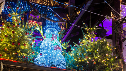 A decorated Christmas tree with colorful lights beside a cheerful snowman wearing a scarf and hat.