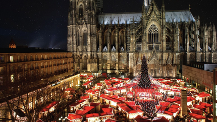 A bustling Christmas market in Cologne, Germany, featuring festive lights, stalls, and visitors enjoying seasonal treats.
