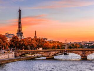 Paris skyline featuring the Eiffel Tower and a bridge, illuminated by the warm hues of sunset.