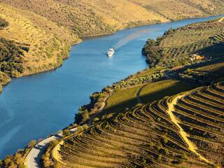 A boat glides down a river surrounded by lush green valley hills under a clear blue sky.