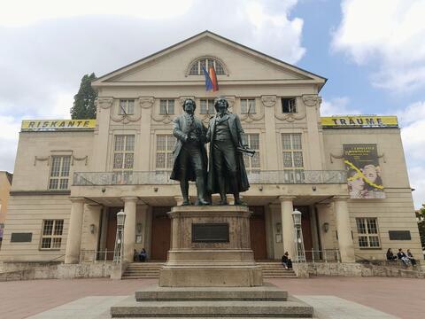 Statue of two men standing in front of the Weimar Theatre building, showcasing historical significance and architectural beauty.