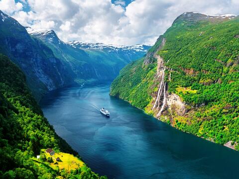 A cruise ship navigates through a scenic fjord in Norway, surrounded by steep cliffs and lush greenery.
