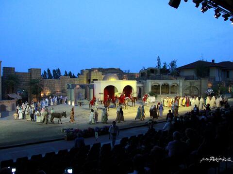 Actors in elaborate costumes perform on stage during the Sordevolo Passion Play, with horses included in the scene.