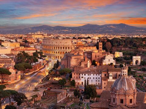 Sunset over Rome, showcasing the silhouette of historic buildings and the warm glow of the sky.