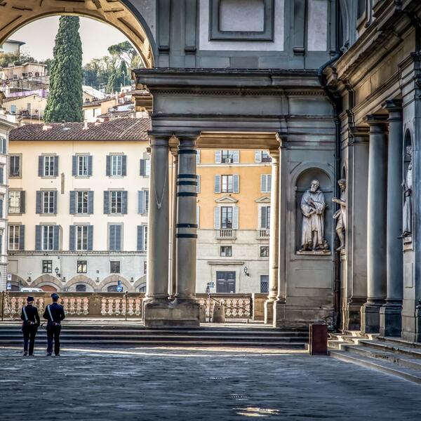 Two individuals stand before the Uffizi Gallery, showcasing its impressive pillar architecture.