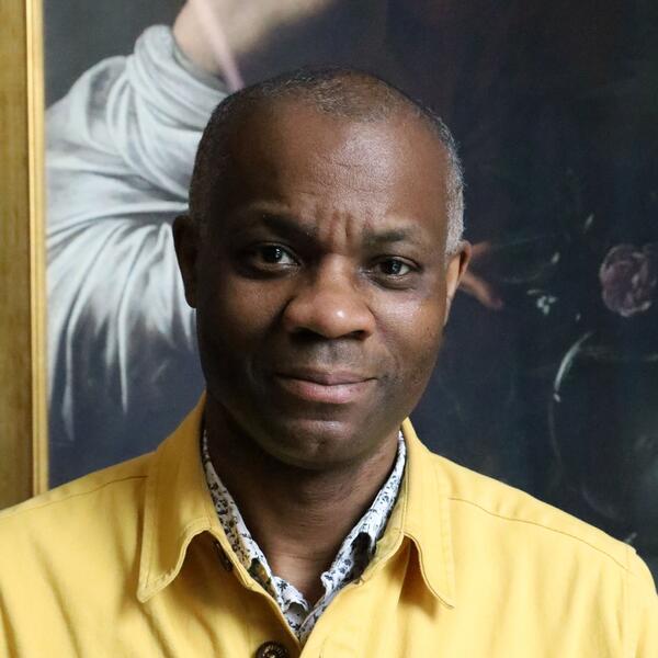 A man wearing a yellow shirt poses in front of a vibrant painting, showcasing his appreciation for art.