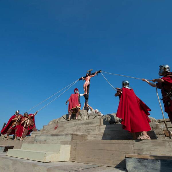 A cast in red costumes stands on a pedestal, showcasing a scene from the Sordevolo Passion Play.