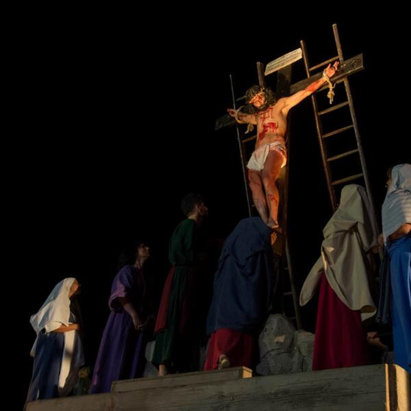 Jesus Christ on the cross during the Sordevolo Passion Play, surrounded by dramatic lighting and somber actors.