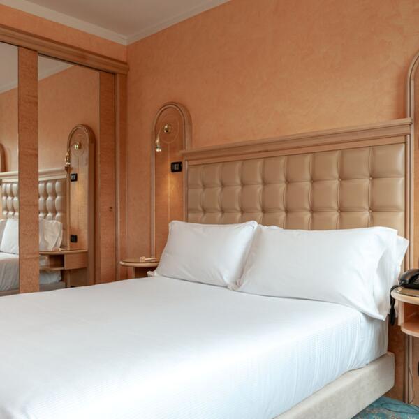 A hotel room featuring a neatly made bed and a large mirror reflecting the space.