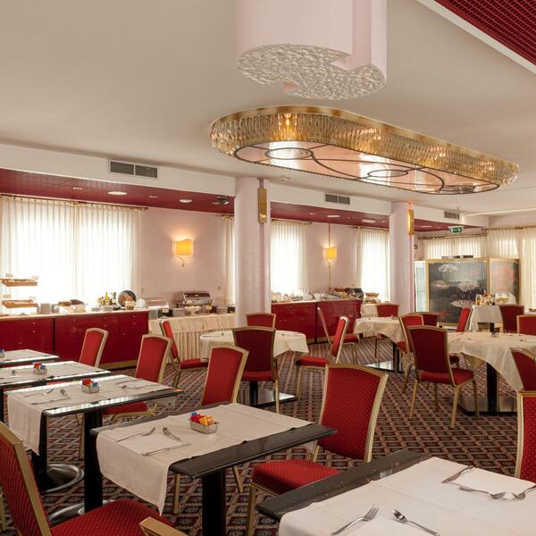 Restaurant interior at Hotel Agora Palace, featuring red chairs and tables arranged for dining.