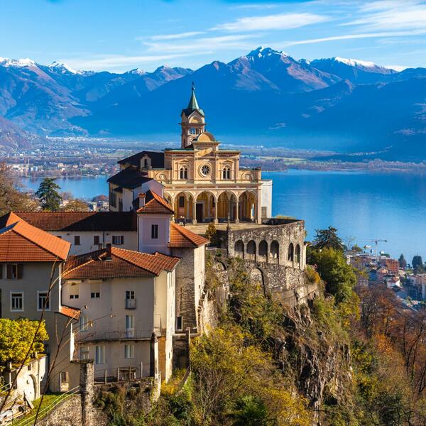 A church perched on a hill, overlooking a serene lake surrounded by lush greenery.