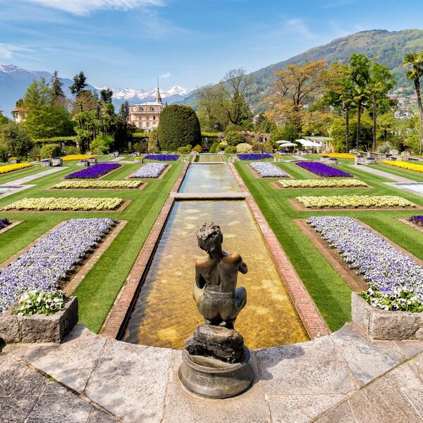 A statue of a person stands amidst vibrant flowers in a lush garden at Villa Taranto.