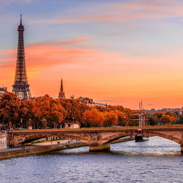 Paris skyline featuring the Eiffel Tower and a bridge, illuminated by the warm hues of sunset.