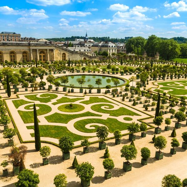 Lush gardens featuring manicured lawns, vibrant flower beds, and classical sculptures under a clear blue sky.
