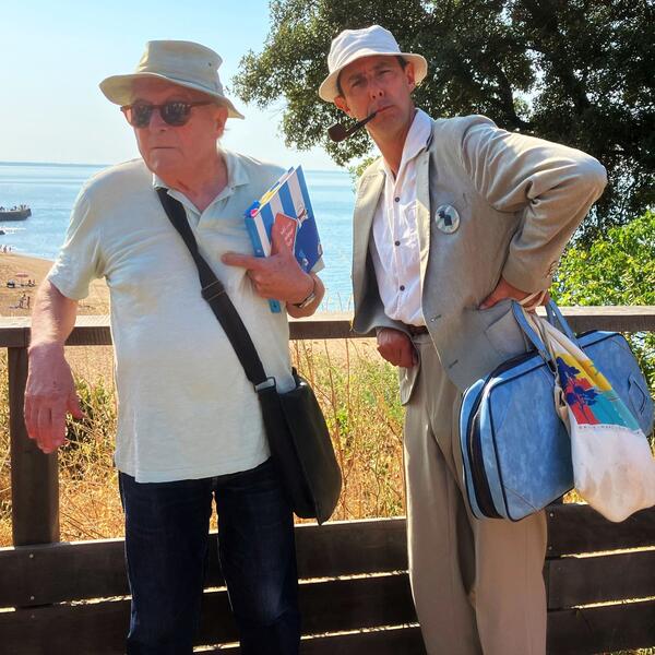Two men stand side by side in a photo; one is in a white shirt, both appear cheerful.