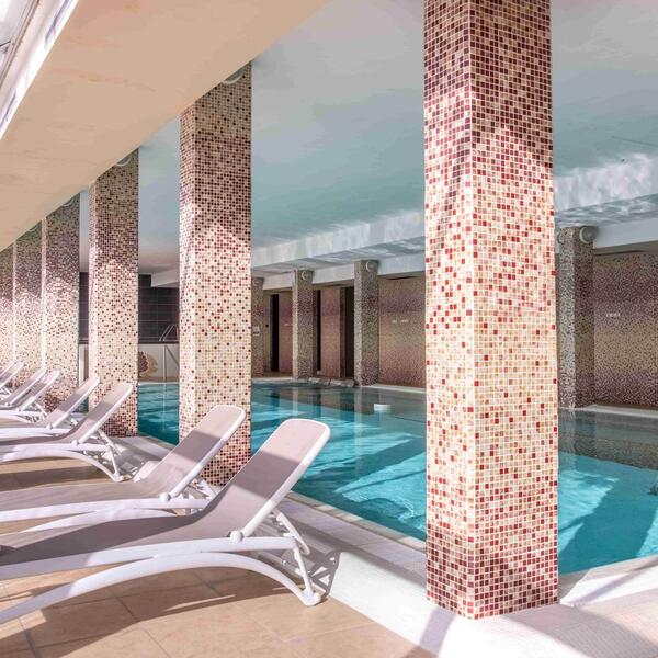 A spacious indoor swimming pool featuring lounge chairs for relaxation along the edges.