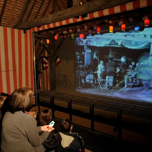 A diverse group of people gathered, watching a movie on a large screen at Maison jour de fête