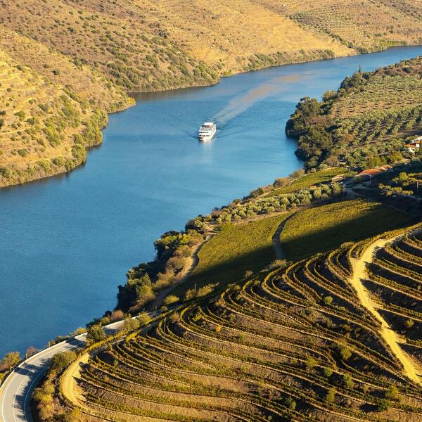 A boat glides down a river surrounded by lush green valley hills under a clear blue sky.