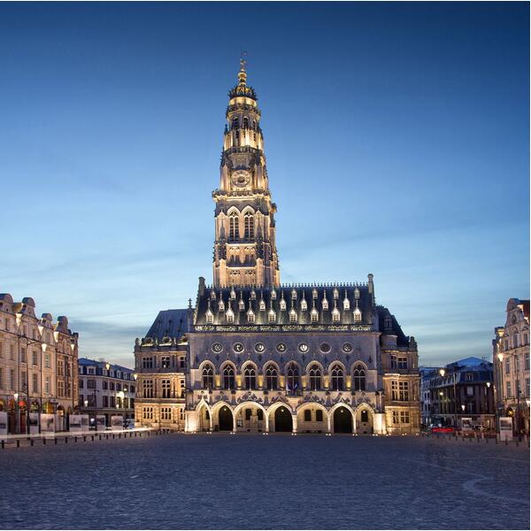 A bustling city square in Arras, featuring the iconic cathedral surrounded by historic buildings and visitors.